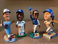 Front view of four Blue Jays bobbleheads on table, showing uniforms and sponsor logos on bases