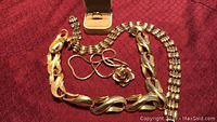 Photo showing two heavy gold plated necklaces, one with large twisted links and one with smaller links and floral pendant, all gold toned. A ring box holding a gold ring also visible.