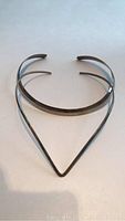Top view of two silver choker necklaces, one rounded band and one V-shaped
