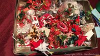 Overhead photo of box filled with assorted Christmas decorations, showing variety of items including bows, wreaths, floral sprays, and ribbons.