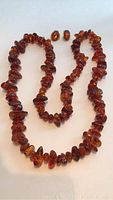 Full shot of amber necklace laid out with matching amber stud earrings above it, showing large polished beads and set studs.