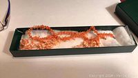 Pair of coral chip bead necklaces laid in a long box with white padding.