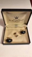 Front view of cuff link set with tie clip inside cream-lined box showing black oval stones and gold-tone metal