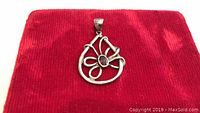 Sterling silver pendant with garnet gemstone center on red background.