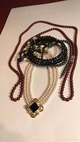 Five costume jewelry necklaces arranged on a white background showing different styles and bead colors including pearls, black and red beads.