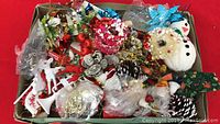 Box with assorted Christmas ornaments including a white snowman, pinecones, artificial berries, and other decorative pieces.
