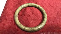 Green jade circular bangle resting on a red textured surface, showing natural veining and color variations.