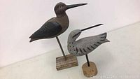 Two wooden shore bird carvings on bases, one larger darker and one smaller gray with markings.