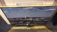 Photo showing one of the large Toronto skyline pictures in a gold metal frame, depicting the cityscape under a clear sky.