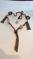 Photo showing the full view of the large necklace and small jade pendant placed on a flat surface with clear visibility of the cord, metal parts, and jade beads.