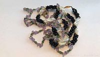 Two necklaces unfolded showing amethyst, jade, mother of pearl, black bead details