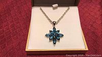 Sterling silver chain necklace displayed in a box with a star pendant made of nine blue topaz gemstones.