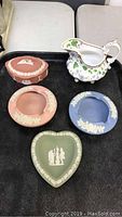 Full view of six pottery pieces including Wedgwood Jasperware items in pink, blue, and green with classical relief and a hand-painted creamer pitcher