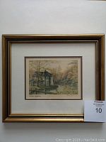 Framed lithograph with gold-tone frame and off-white matting. Visible artwork with autumnal house scene.