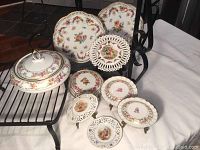 Photo showing full set including lidded candy dish, reticulated plates, and smaller decorative plates arranged on metal rack and glass shelf.