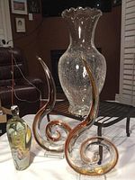 Photo showing two swirl-shaped glass sculptures, one visibly 8.5-inch signed Brian Ashby abstract heavy piece with amber and clear glass, and a tall clear crackle glass ruffle vase behind them.