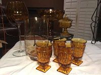 Collection of amber glass and crystal items on a white tablecloth, includes goblets and footed vases.