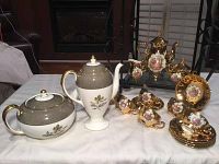 Full view of the porcelain tea set with gold plating and floral decor including teapot, sugar bowl, creamer, cups and saucers.