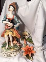 Front view of the 16-inch Capodimonte porcelain figurine seated with basket of flowers and the two Birks porcelain flower figurines.