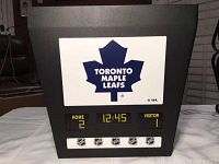 Front view of the light fixture showing Toronto Maple Leafs logo, digital home and visitor score display, timer, and NHL logos