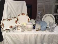 Full arrangement of vintage Royal Albert Old Country Rose china, Wedgwood, Limoges, Coalport, and crystal pieces on white cloth background