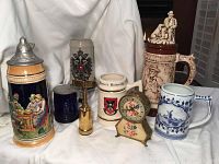 Photo showing all items in lot including German beer steins, mugs, clock, and bottle opener arranged on white cloth.