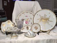 Group photo showing porcelain plates, leaf-shaped serving pieces, crystal vase, and teacup with saucer arranged on a cloth background.