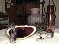 Lot of signed perfume bottle and art glass items on a white table, includes amethyst vase, purple decorative perfume bottle, oval dish and sculptural purple bowl