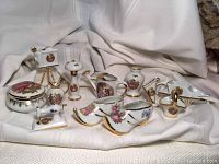 Photo showing all 12 Limoges porcelain miniatures arranged on white fabric background, highlighting the intricate gold and floral detailing on each item.