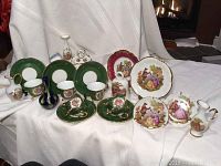 Full set of Limoges porcelain miniatures including 5 green teacups and saucers, decorative plates, clock, bell, vase, and water pitcher arranged on white fabric.