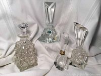 Four crystal perfume bottles arranged on white fabric. Includes German Lausitzer Glas with original green sticker, Bohemian Czech Art Deco bottle, and two MCM cut crystal bottles with geometric stoppers.