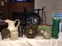 Display of multiple pottery and stoneware pieces on white cloth in front of fireplace.