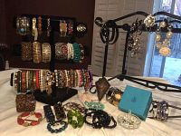 Overall display of vintage and costume jewelry including bracelets, bangles, earrings, brooch, watch, and ring holder arranged on stands and flat surfaces
