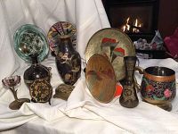 Wide shot of all 11 decorative items including glass candleholder, brass plates, vases, mugs, and etched glass bowl arranged on white cloth.