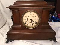Full view of antique wooden mantel clock with claw feet, clock face shows Roman numerals, clock has handles on either side