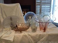 Full lot view on white cloth backdrop including various glass plates, bowls, and vase arranged with fireplace and window behind
