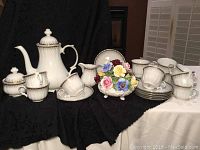 Overview photo showing entire tea set and floral bouquet arranged on black fabric.