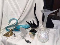 Lot of assorted figurines displayed on white draped cloth, featuring hand-painted blue glass swan, black glass swan, brass duck, and smaller figurines in front
