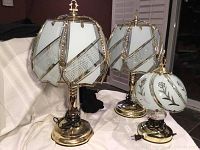 Pair of 22 inch metal and frosted glass panel lamps with gold-tone metal and geometric designs, standing next to 14 inch floral frosted glass touch sensor lamp on a white surface.