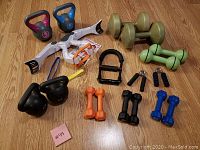 Overview of all workout equipment including kettlebells, dumbbells, and hand grips placed on a wooden floor