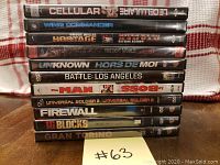 Stack of 11 action DVDs showing titles on spines: Cellular, Wing Commander, Hostage, The Lost World, Unknown, Battle: Los Angeles, The Man, Universal Soldier 2, Firewall, 16 Blocks, Gran Torino.