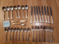 Full set of silverware laid out on a wood surface: 6 teaspoons, 12 knives, 6 forks, 12 soup spoons, 2 small forks, and 2 small spoons.