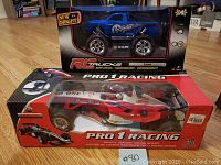Photo showing two radio control vehicles in original packaging: a blue RAM branded RC truck and a red and white Pro 1 Racing Formula 1 style RC car.