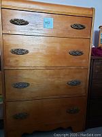 Front view of the tall solid wood dresser showing four drawers with paired decorative metal handles and the top edge curve.