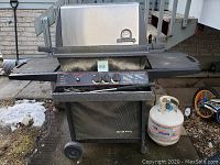 Full view of Broil King gas BBQ grill on cart with side shelves and propane tank beside it.