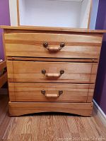 Front view of solid wood dresser showing 3 drawers with wooden and metal handles.