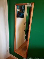 Full-length wooden framed mirror hanging on a green wall, showing reflection of a doorway and room corner.