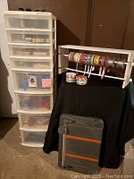 Plastic drawer storage unit beside a ribbon holder with multiple ribbons and a folded black cloth on a stand, plus Friskars paper cutter leaning against the stand.