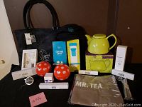 Photo showing full lot items including purse, teapot, red spherical tea infusers, apron, packaged spoons and infuser boxes