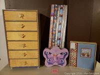 Wooden storage drawer system with six drawers and hand-shaped pulls next to gift wraps, puzzle, and memory book.